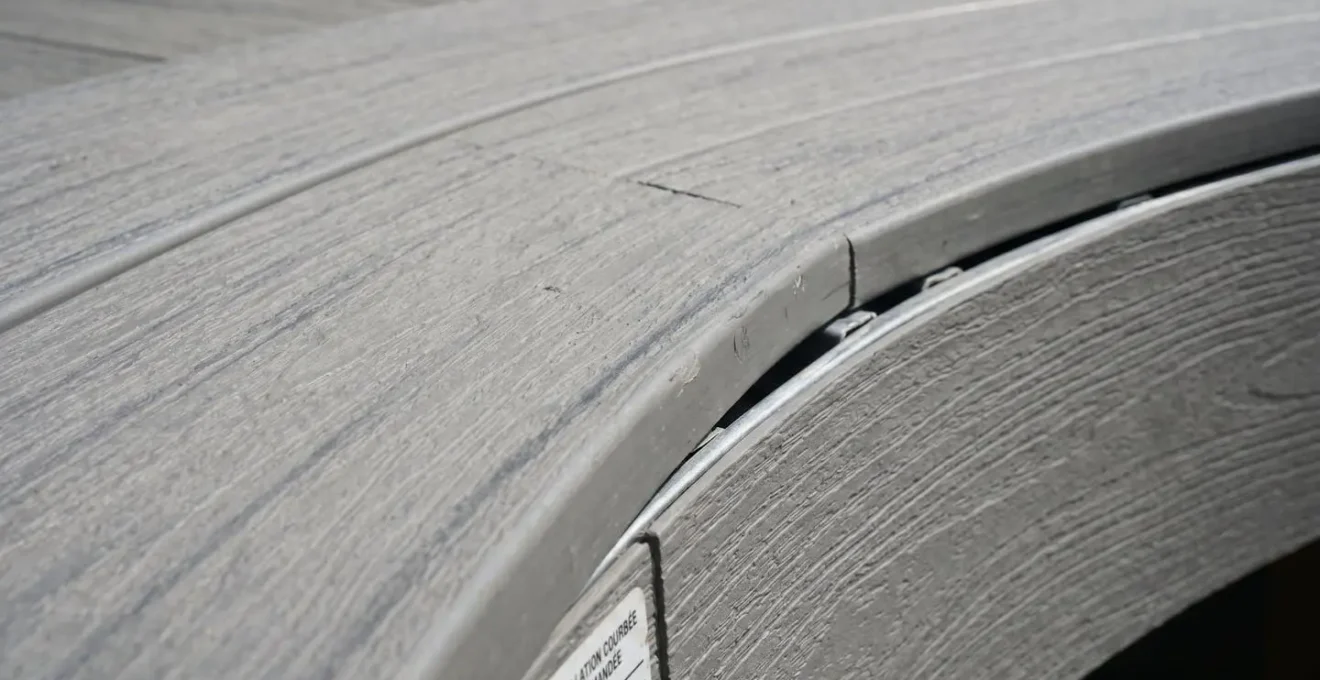 Détail macro d'une planche de terrasse en PVC gris courbée montrant le rayon de courbure uniforme et la texture composite du matériau